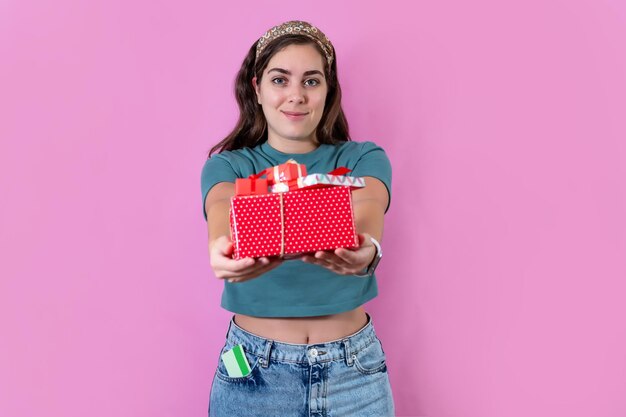 Menina segurando nas mãos uma caixa de presentes isolada sobre fundo rosa pastel