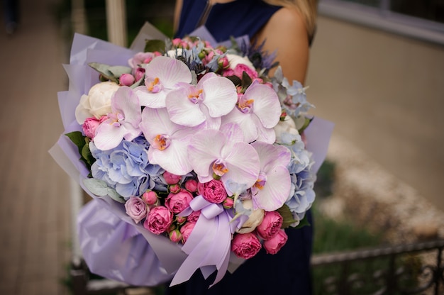 Menina segurando o buquê de orquídeas rosa pastel e rosas e hortênsia azul