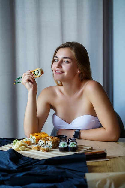 Menina segurando o rolo de sushi de pauzinhos. Jovem comendo sushi delicioso.