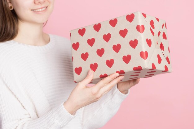 Menina segurando presente com corações no conceito de dia dos namorados de fundo rosa