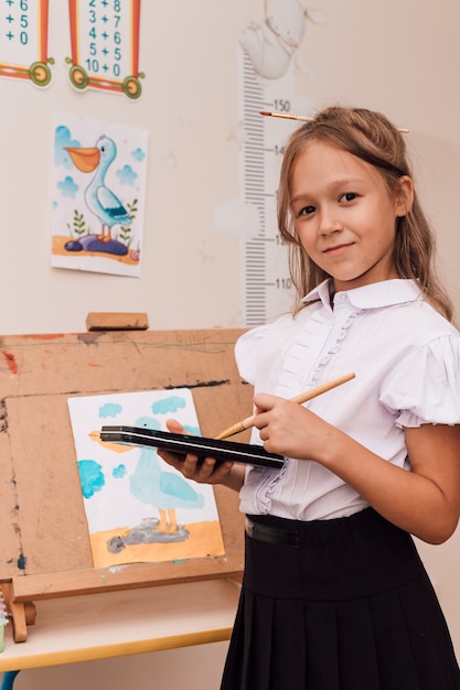 Menina segurando tintas e um pincel nas mãos