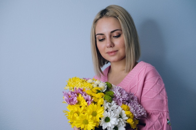 Menina segurando um buquê de flores nas mãos. Fundo claro, retrato do close-up. Conceito de feriado, aniversário, dia da mulher.