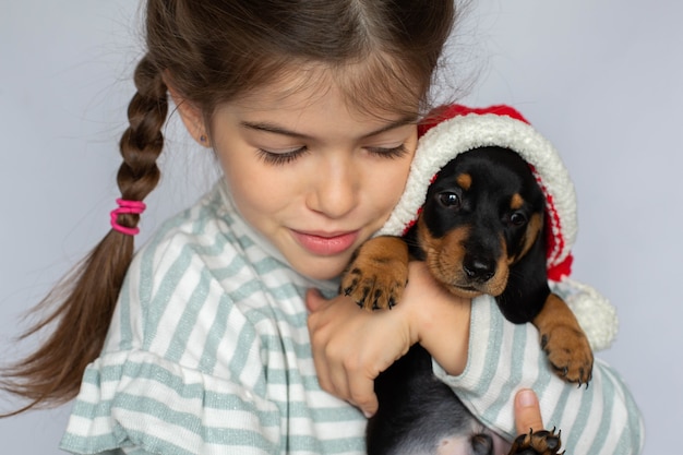 Menina segurando um cachorrinho bassê em seu presente de ano novo com chapéu de Papai Noel