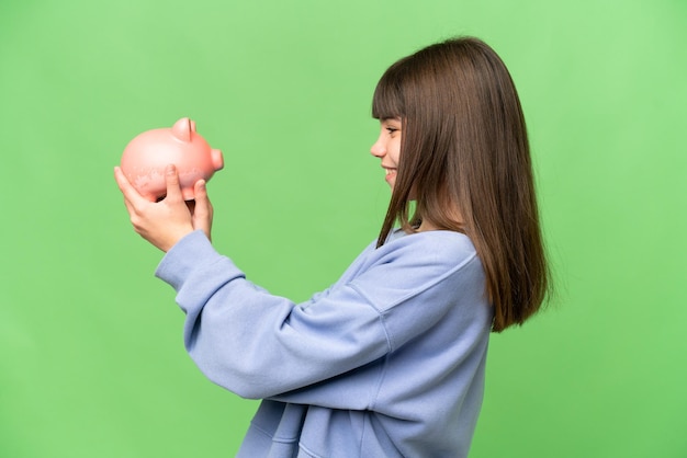 Menina segurando um cofrinho sobre fundo croma chave isolado com expressão feliz