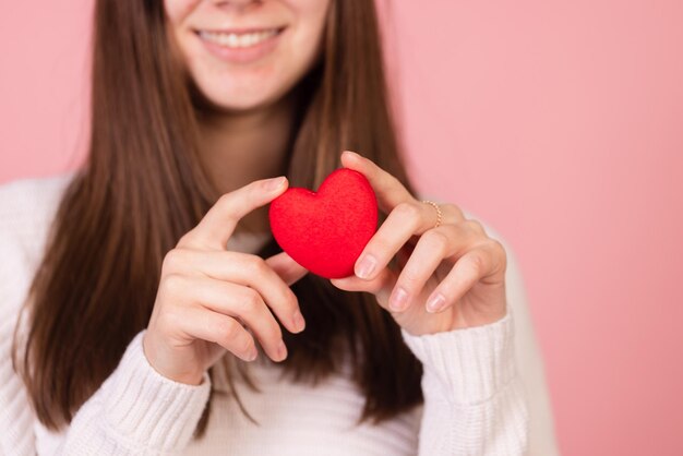 Menina segurando um coração em suas mãos closeup em um fundo rosa o conceito de dia dos namorados