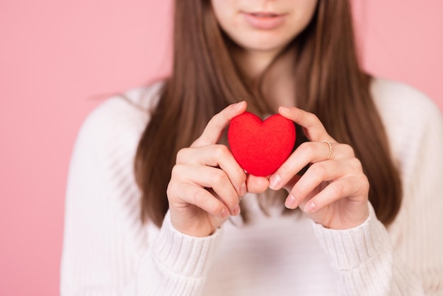 Menina segurando um coração em suas mãos closeup em um fundo rosa o conceito de dia dos namorados