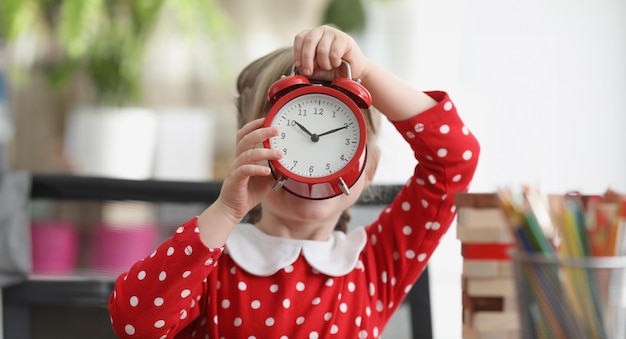 Foto menina segurando um despertador vermelho na frente de seu rosto