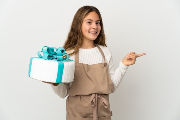 Menina segurando um grande bolo sobre um branco isolado apontando o dedo para o lado