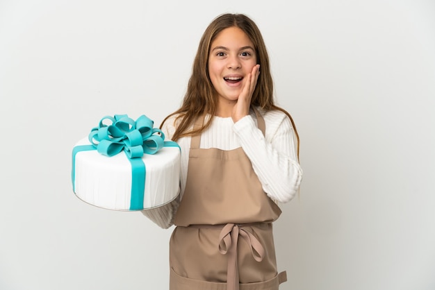 Menina segurando um grande bolo sobre um fundo branco isolado com expressão facial surpresa e chocada