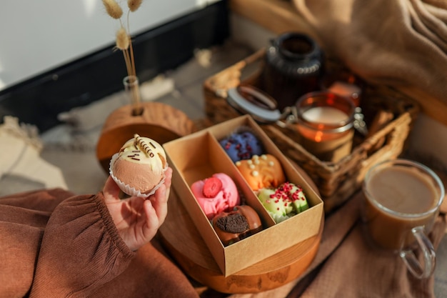 Menina segurando um macaron na mão com uma caixa de macarons variados ao fundo em um ambiente aconchegante em casa