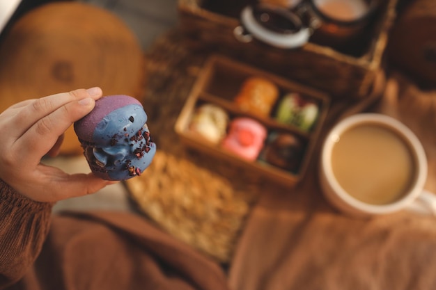 Menina segurando um macaron na mão com uma caixa de macarons variados ao fundo em um ambiente aconchegante em casa