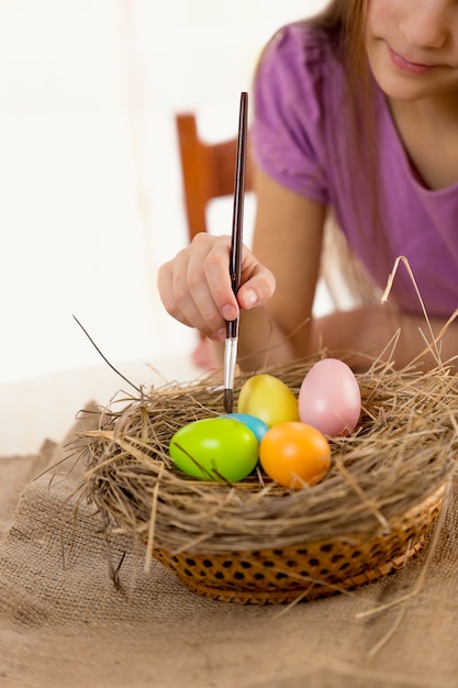 Menina segurando um pincel e colorindo ovos de Páscoa