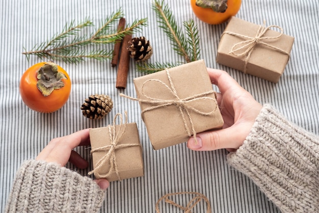 Menina segurando um presente embalado com as próprias mãos, close-up. Decoração de Natal, desenho de uma caixa de presente para o Natal feita de materiais naturais. Atmosfera de ano novo, preparação para o Natal.