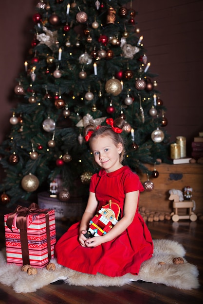 Menina segurando um quebra-nozes perto da árvore de Natal