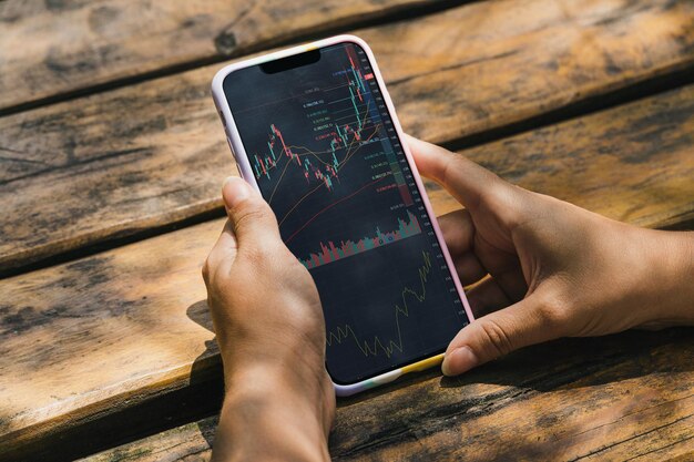 Menina segurando um smartphone com gráfico do mercado financeiro de ações na tela do parque. Bolsa de Valores.