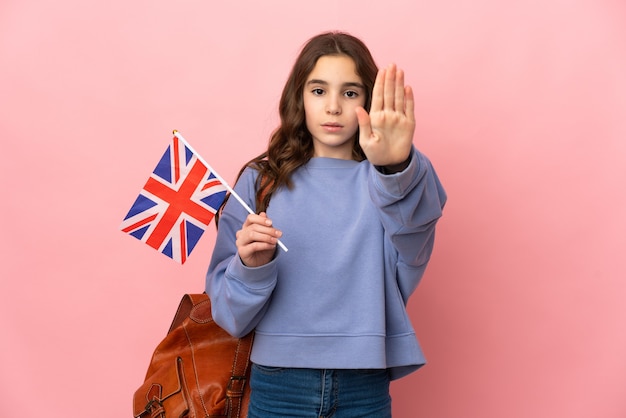 Menina segurando uma bandeira do Reino Unido isolada em um fundo rosa, fazendo um gesto de pare