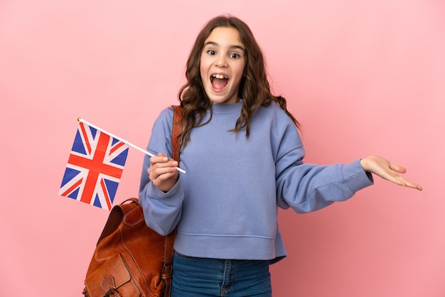 Menina segurando uma bandeira do Reino Unido isolada na parede rosa com expressão facial chocada