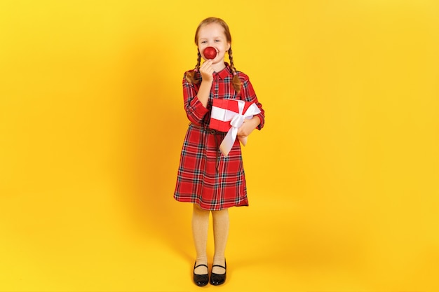 Menina, segurando uma caixa com um presente e fazendo o nariz de uma bola de natal.