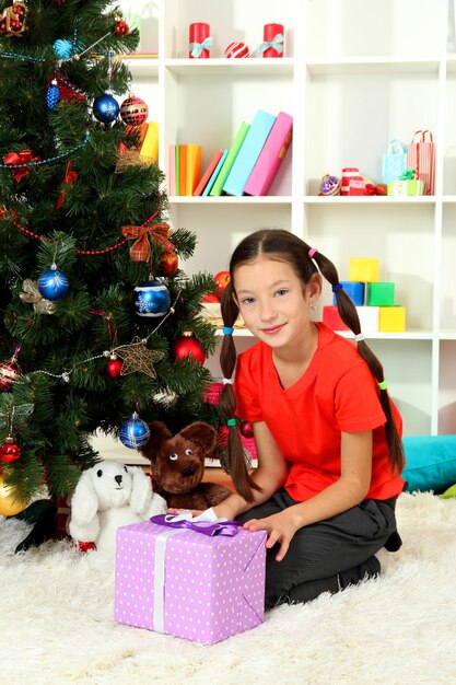 Menina segurando uma caixa de presente perto da árvore de Natal