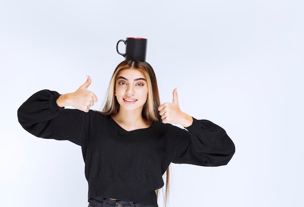 Menina segurando uma caneca de café preta na cabeça e se sentindo satisfeita. Foto de alta qualidade