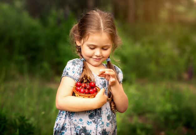 menina, segurando uma cesta de cerejas na natureza no verão