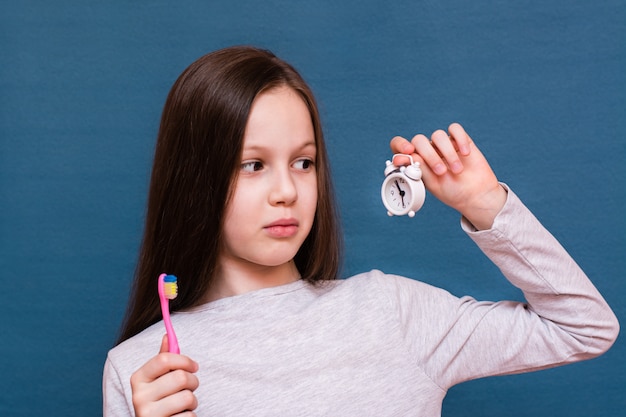 Menina segurando uma escova de dentes e um despertador