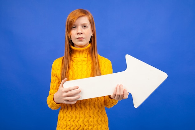 Menina segurando uma flecha de papel como um ponteiro para a direita em um fundo azul