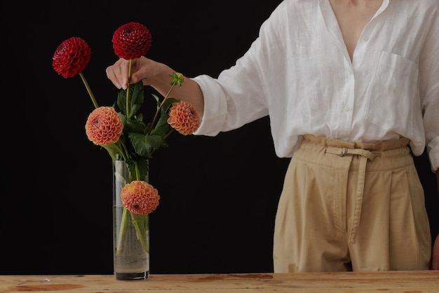 Menina segurando uma flor dália em um vaso de vidro em uma maquete de fundo escuro de mesa de madeira