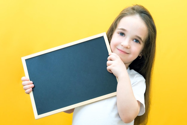 Menina segurando uma folha de placa Menina bonitinha com espaço de cópia de fundo amarelo de quadro de giz