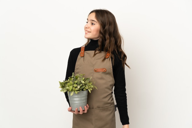 Menina segurando uma planta isolada no fundo branco, olhando para o lado e sorrindo