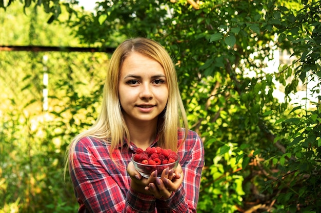 Menina segurando uma tigela com produto orgânico de framboesas maduras na fazenda.