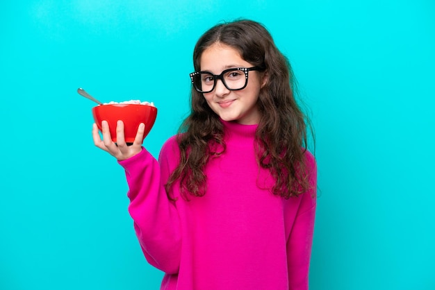 Menina segurando uma tigela de cereais isolada em fundo azul sorrindo muito