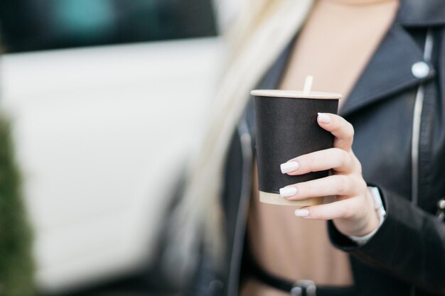 Menina segurando uma xícara de papelão Xícara de café de papel em uma mão de mulher no fundo da loja Bebida quente Mão segurando uma xícara de café de papel Xícara de café de papel