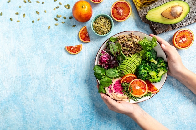 Menina segurando vegan, tigela de desintoxicação de buda com frutas, vegetais e sementes sobre um fundo azul. espaço para texto.