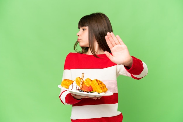 Foto menina segurando waffles sobre fundo chave de croma isolado fazendo gesto de parada e decepcionado