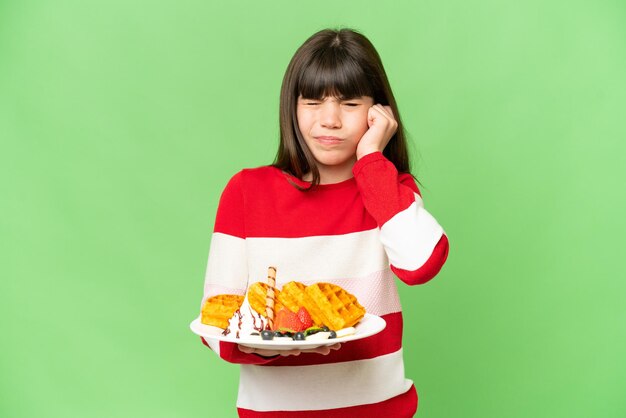 Menina segurando waffles sobre fundo croma isolado frustrado e cobrindo as orelhas
