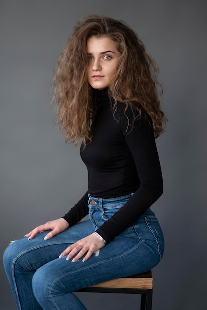 Foto menina sensual com cabelo encaracolado, sentado na cadeira alta em um fundo cinza