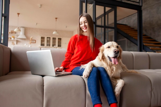 Menina senta no sofá com cachorro e usa laptop em casa mulher com golden retriever olha para o computador