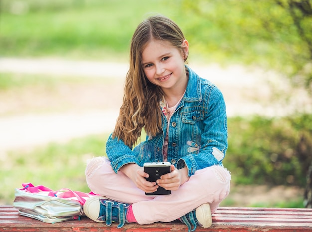 Menina senta-se com o telefone no parque