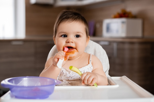 Foto menina senta-se na cadeira de uma criança comendo purê de legumes