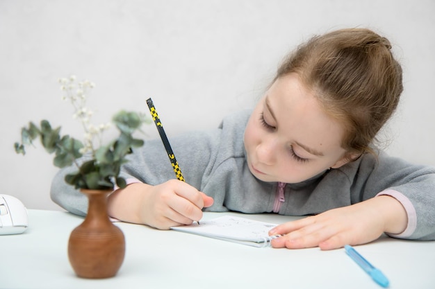 Menina sentada à mesa com concentração e escreve diligentemente em um caderno de volta à escola