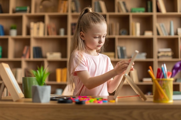 Menina sentada à mesa com placa fazendo palavras de letras coloridas exercitando em aulas de desenvolvimento infantil