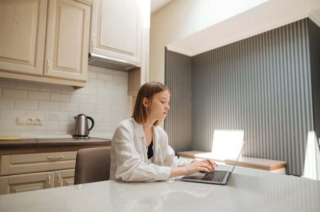 Menina sentada à mesa da cozinha usando um laptop