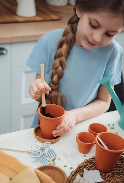 Menina sentada à mesa em casa semeando sementes em vasos de flores Jardinagem em casa