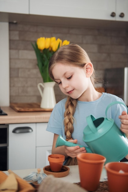 Menina sentada à mesa em casa semeando sementes em vasos de flores Jardinagem em casa