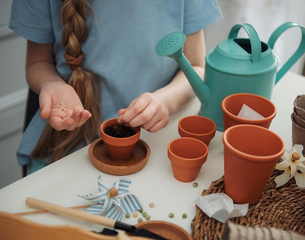 Menina sentada à mesa em casa semeando sementes em vasos de flores