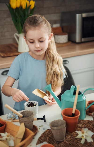 Menina sentada à mesa em casa semeando sementes em vasos de flores