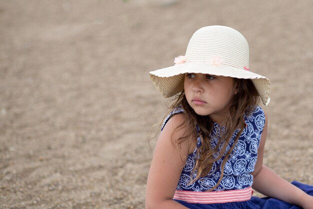 Menina sentada com chapéu de verão e lindo vestido na praia