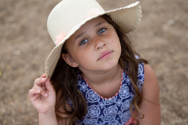 Menina sentada com chapéu de verão e lindo vestido na praia