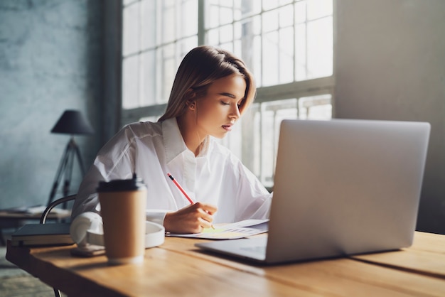 Menina sentada concentrada no laptop e estudando remotamente.